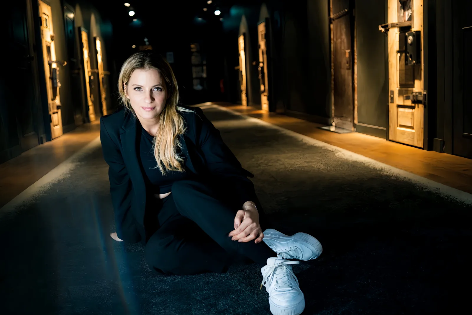 Rebecca Steinbach sitzt in schwarzem Anzug und weißen Sneakern in einem beleuchteten Gewölbegang